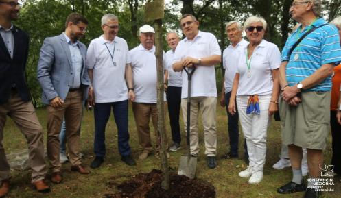 Grupa osób stoi przy drzewie.