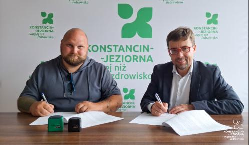 Dwóch mężczyzn siedzi przy biurku i podpisuje dokumenty.