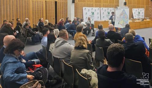 Grupa ludzi siedzi na krzesłach w sali konferencyjnej i słuch prezentacji.