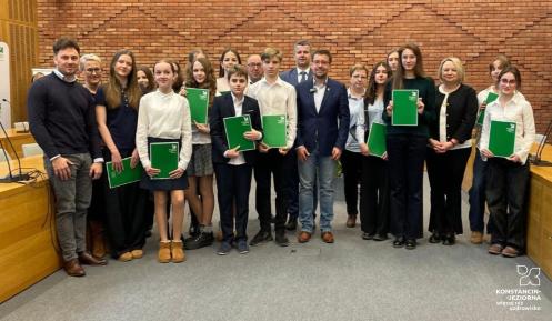 Grupa osób pozuje do zdjęcia na tle ściany z czerwonej cegły