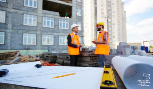 Dwóch robotików na tle budowy bloku mieszkalnego.