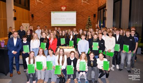 Uczestnicy gali sportowej wraz z burmistrzem Michałem Wiśniewskim pozują do wspólnego zdjęcia zbiorowego.