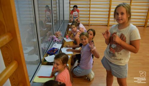 Zdjęcie grupy uśmiechniętych dzieci rysujących w sali gimnastycznej.