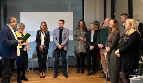 Grupa osób stoi w sali urzędu podczas świątecznego spotkania, w trakcie którego wręczane są podziękowania członkom Rady Seniorów.