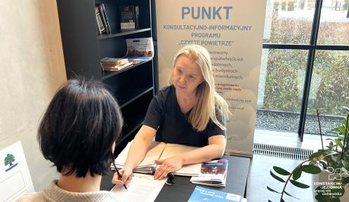 Dwie kobiety siedzą naprzeciwko siebie. Jedna z nich pokazuje drugiej dokument.