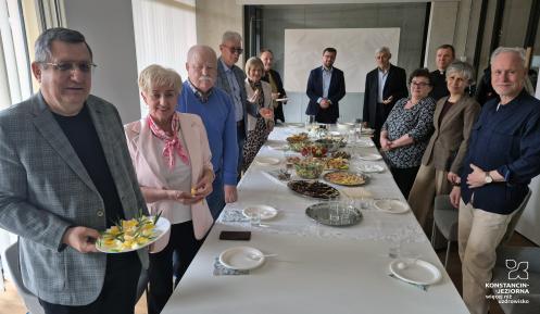 Burmistrz Michał Wiśniewski i przewodniczący Rady Seniorów Wojciech Guszkowski stoją przy stole z grupą seniorów podczas spotkania przedświątecznego w urzędzie gminy.