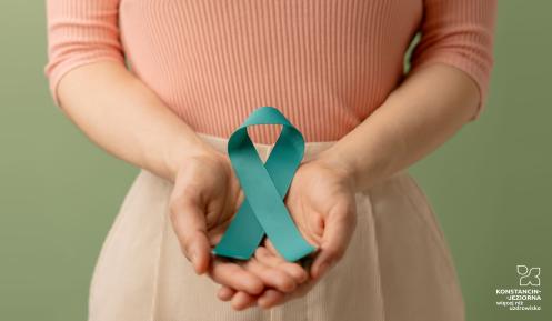 Kobieta trzyma w otwartych dłoniach jasnoturkusową wstążkę, która jest symbolem profilaktyki raka szyjki macicy. Tło jest neutralne, w odcieniach zieleni, co podkreśla przesłanie dbałości o zdrowie.