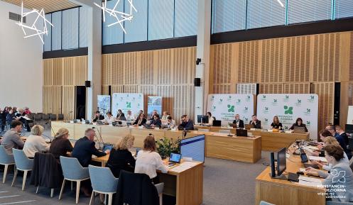 Grupa osób siedzi za stołami na sali posiedzeń.