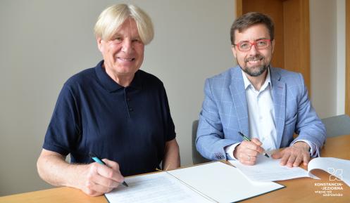 Dwóch mężczyzn siedzi przy stole i podpisuje dokumenty podczas zawarcia porozumienia dotyczącego współpracy Muzeum Villa la Fleur z Konstancińską Kartą Mieszkańca.