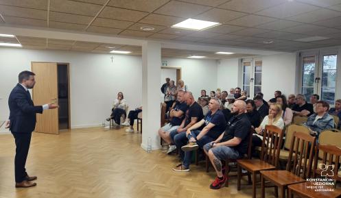 Grupa osób w sali świetlicowej słucha wystąpienia burmistrza