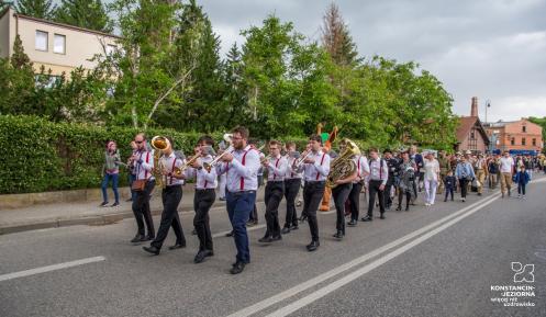 Orkiestra dęta maszeruje ulicą, a za nią tłum mieszkańców