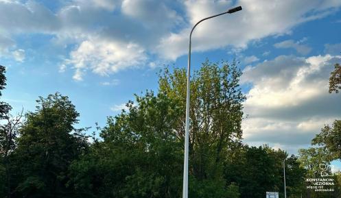 Na zdjęciu widać nowo zamontowaną latarnię uliczną przy ul. Literatów. Słup z oprawą LED stoi przy jezdni w pobliżu przystanku autobusowego, a w tle znajdują się drzewa i chodnik. Nowe oświetlenie poprawia bezpieczeństwo i widoczność po zmroku.