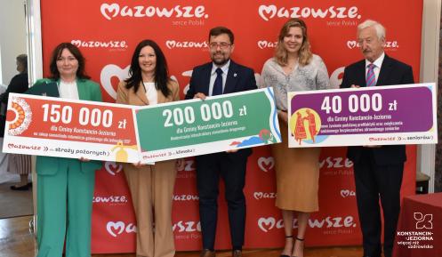 Cztery osoby trzymających w rękach symboliczne czeki z kwotami dofinansowania.
