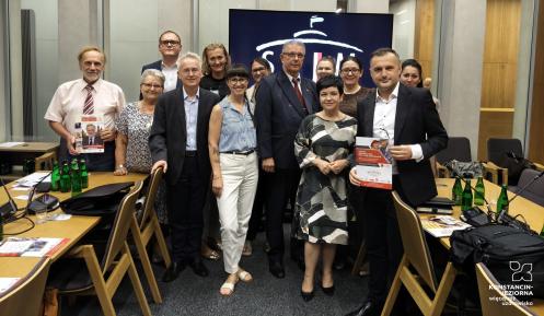 Grupa uczestników posiedzenia Parlamentarnego Zespołu ds. Seniorów pozuje do wspólnego zdjęcia w sali obrad.