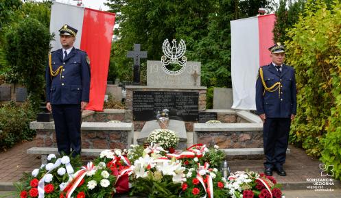 Dwóch strażników miejskich pełni wartę przy nagrobku na cmentarzu.