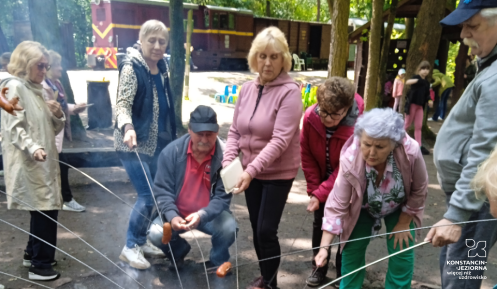 Grupa seniorów piecze kiełbaski nad ogniskiem