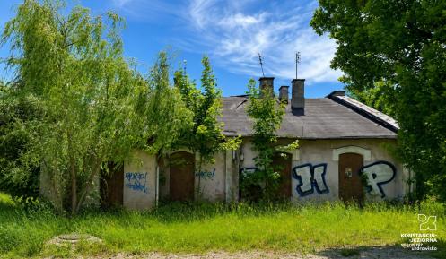 Zaniedbany budynek dawnej parowozowni z zamurowanymi oknami i graffiti na ścianach. Obiekt otaczają wysoka trawa i drzewa