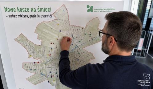 Mężczyzna przypina kolorową pinezkę do mapy gminy Konstancin-Jeziorna, wskazując proponowaną lokalizację nowego kosza na śmieci.