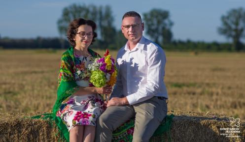 Kobieta i mężczyzna siedzą na beli skoszonego siana i wspólnie trzymają bukiet kwiatów. To starostowie dożynek 2026
