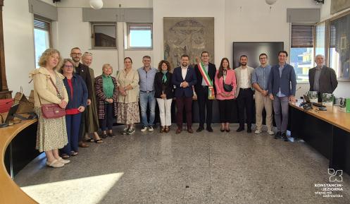 Grupowe zdjęcie delegacji Konstancina-Jeziorny i przedstawicieli Pisogne wykonane w sali posiedzeń włoskiego ratusza. W centrum stoi burmistrz Pisogne w szarfie w barwach włoskiej flagi, obok przedstawiciele obu miast.