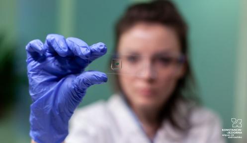 Zdjęcie przedstawia osobę w rękawiczkach laboratoryjnych analizującą próbkę na szkiełku pod mikroskopem.