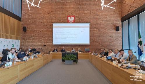 Grupa osób siedzi za stołami na sali posiedzeń
