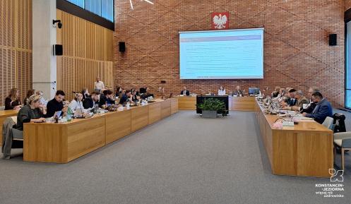 Sala obrad Rady Miejskiej Konstancin-Jeziorna podczas sesji. Radni siedzą przy stołach i uczestniczą w posiedzeniu.