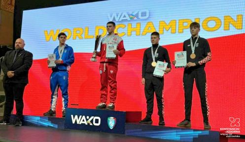 Kamil Kraczkowski , reprezentant Polski, odbiera złoty medal podczas ceremonii dekoracji na Mistrzostwach Świata WAKO. Zawodnicy stoją na podium na tle wielkiego ekranu z napisem "WAKO WORLD CHAMPION".