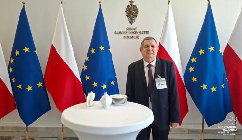 zdjęcie Wojciecha Guszkowskiego na tle flag Polski i UE