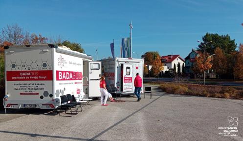 Przed urzędem stoją dwa mobilne gabinety medyczne oznaczone napisem „Badabus”, przy których znajdują się pracownicy oraz krzesła dla oczekujących pacjentów.