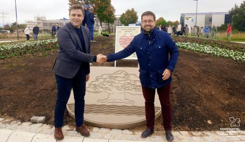 Burmistrzowie Michał Wiśniewski i Fabian Nitz ściskają dłonie na nowym rondzie w Denzlingen, przed kamiennym herbem Konstancina-Jeziorny. W tle tablica partnerska i uczestnicy uroczystości.