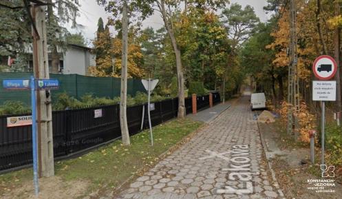 Ulica Łąkowa z nawierzchnią z betonowej trylinki, otoczona drzewami i ogrodzeniami, z widocznym oznakowaniem drogowym oraz zaparkowanym białym samochodem dostawczym.