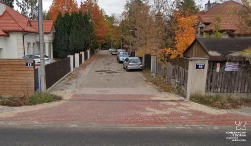 Widok wewnętrznego odcinka ul. Kazimierza Pułaskiego z kostką brukową, zaparkowanymi samochodami i jesiennymi drzewami wzdłuż posesji.
