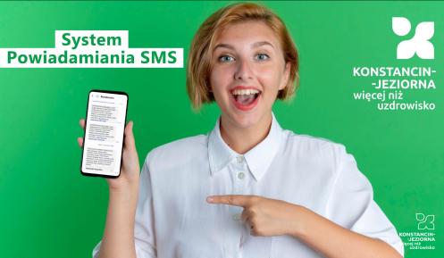Uśmiechnięta młoda kobieta na zielonym tle trzyma w dłoni smartfon z wiadomościami SMS i wskazuje na niego palcem. Na grafice widnieje napis „System Powiadamiania SMS” oraz logo „Konstancin-Jeziorna więcej niż uzdrowisko”.