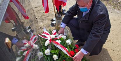 Mężczyzna przyklęka przed tablicą na pomniku, składa wiązankę ozdobioną biało-czerwonymi kwiatami
