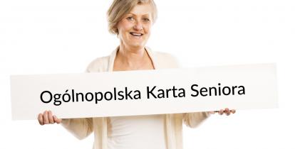 Na zdjęciu uśmiechnięta seniorka, która w rękach trzyma dużą kartę papieru, na której znajduje się napis - Ogólnopolska Karta Seniora. 