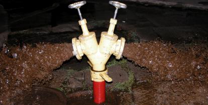 Stojak z dwiema głowicami podłączony do hydrantu wystającego z gruntu, z głowic wylewają się nieczystości