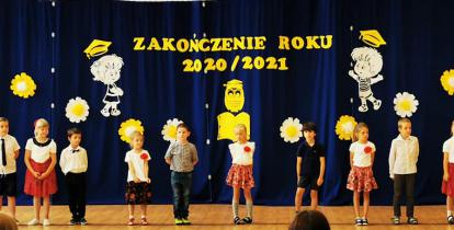 Grupa dzieci na Sali gimnastycznej podczas przedstawienia na zakończenie roku szkolnego, na pierwszym planie publiczność. 