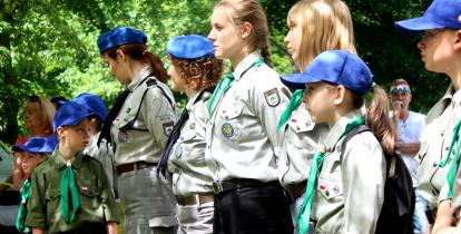 Grupa dzieci i młodzieży w strojach harcerskich podczas musztry.