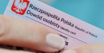 Fragment dowodu osobistego, który w palcach trzyma kobieta. Widoczna jest tylko jej dłoń. 