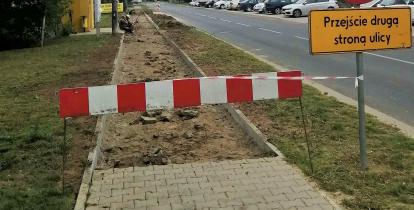 Remont chodnika. Na pierwszej części chodnika położona jest kostka brukowa, dalej widać ziemie, na której dopiero będzie ona kładziona. Wejście na chodnik jest ogrodzone, biało czerwonym szlabanem.