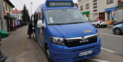Niebieski bus stoi na przystanku, ma otwarte boczne drzwi, nad przednią szybą wyświetlacz z numerem linii L16 i nazwami przystanków – początkowego i końcowego – Czarnów.
