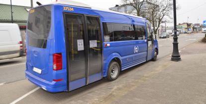 Niebieski autobus niskopodłogowy odjeżdża z przystanku, w tle budynki i ulica.