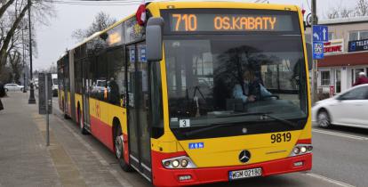 Ulica, po której jedzie czerwono-pomarańczowy autobus komunikacji miejskiej. Nad jego przednią szybą wyświetla się napis: 710 Osiedle Kabaty.