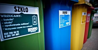 Zdjęcie przedstawia pięć dużych pojemników na śmieci segregowane. Ustawione są obok siebie, różnią się kolorami (od lewej: zielony, niebieski, żółty, czerwony, zielony).
