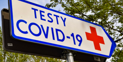 Tabliczka informacyjna. Na białym tle niebieski napis – testy na covid-19. Obok czerwony znak krzyża. 