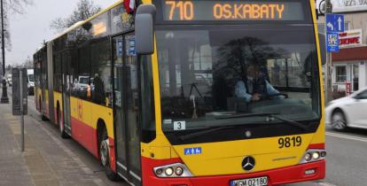 Ulica, po której jedzie czerwono-pomarańczowy autobus komunikacji miejskiej. Nad jego przednią szybą wyświetla się napis: 710 Osiedle Kabaty.