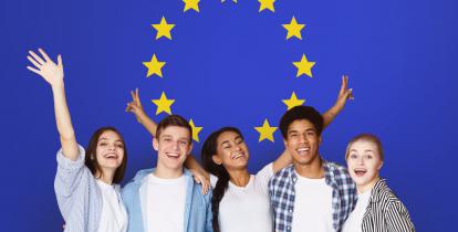 Grupa uśmiechniętych uczniów (5 osób, w tym trzy kobiety) na tle flagi Unii Europejskiej (okrąg złożony z dwunastu złotych gwiazd na błękitnym tle).
