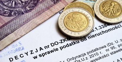 Na decyzji podatkowej leżą banknoty (20 złotych i 10 złotych) i monety (dwie monety po 5 złotych i 1 moneta 2 złotowa).