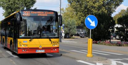 Ulica, po której jedzie czerwono-pomarańczowy autobus komunikacji miejskiej. Nad jego przednią szybą wyświetla się napis: 200 Konstancin-Jeziorna.